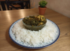 A bowl of creamy palak chicken curry made with spinach, tender chicken, and aromatic spices, served with naan and rice.